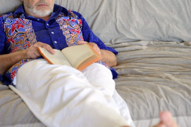 senior holding a book and sleeping on the couch The Negative Effects Of Sleeping While Sitting For Seniors