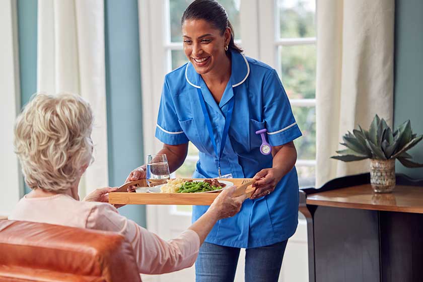 Female Care Worker In Uniform Bringing Meal On Tray