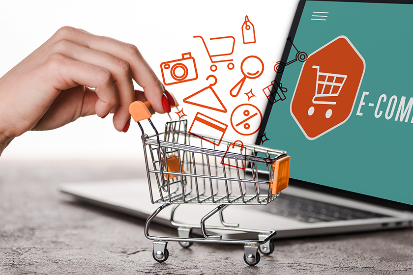 Cropped view of woman holding toy shopping cart near laptop and illustration on white, e-commerce concept