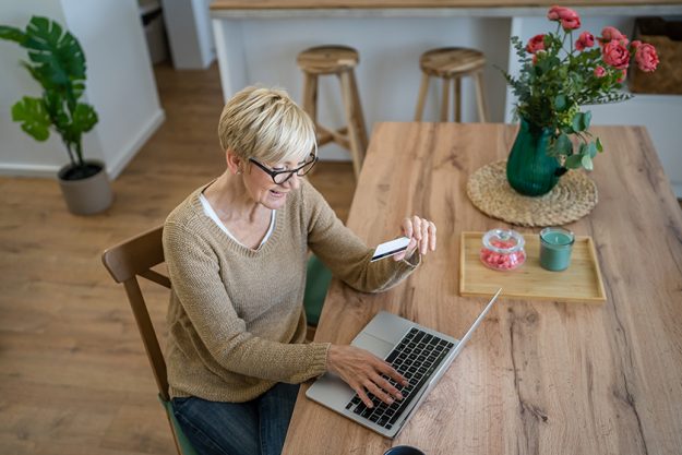 One mature senior woman grandmother sit at home use credit or debit card for online shopping browse internet stores use laptop computer buying stuff real people copy space