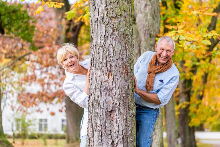 Senior couple flirting playing around tree in park Senior couple flirting playing around tree in park