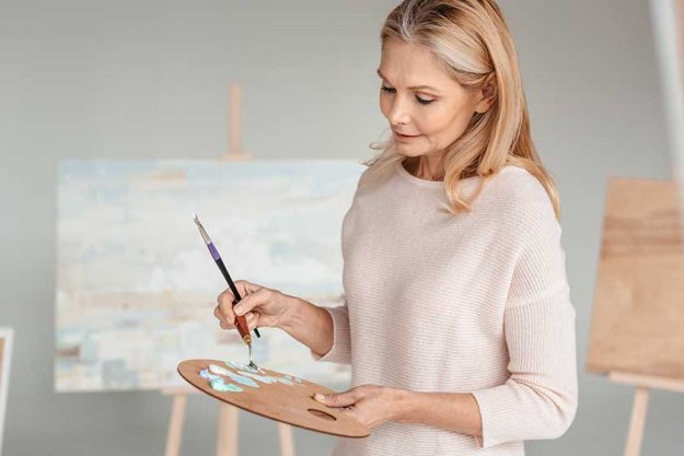 Mature woman holding palette and paintbrush in art studio Mature woman holding palette and paintbrush in art studio