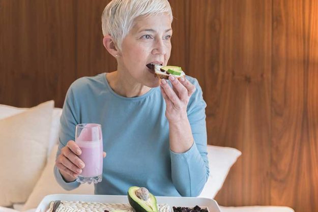 Portrait of beautiful senior woman drinking pink fruit smoothie and eating healthy toast with avocado Portrait of beautiful senior woman drinking pink fruit smoothie and eating healthy toast with avocado
