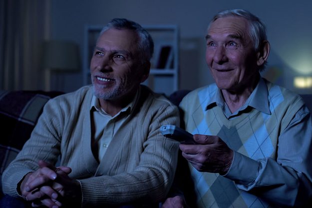 Happy aged men watching tv at night holding remote-control Happy aged men watching tv at night holding remote-control