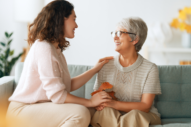 Happy adult woman and her senior mother with autumn leaves indoors Happy adult woman and her senior mother with autumn leaves indoors
