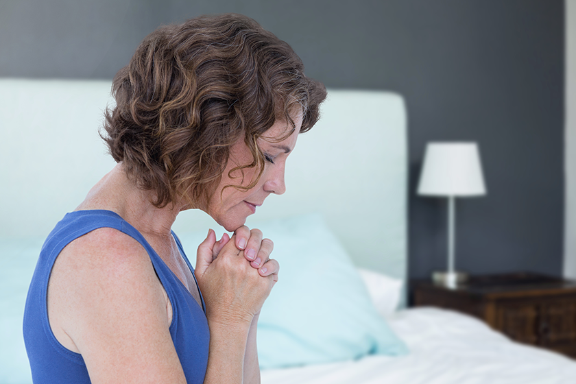 Woman praying hopeful and sad next to bed Woman praying hopeful and sad next to bed