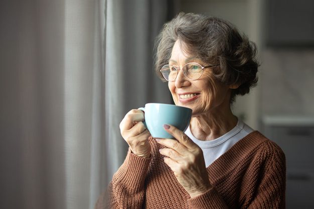 Happy senior woman drinking coffee looking out window Happy senior woman drinking coffee looking out window
