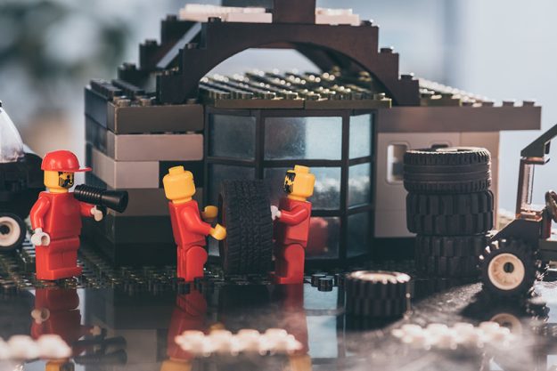 KYIV, UKRAINE – MARCH 15, 2019: lego minifigures in red carrying tire while other figurine shouting in mouthpiece at service station KYIV, UKRAINE - MARCH 15, 2019: lego minifigures in red carrying tire while other figurine shouting in mouthpiece at service station