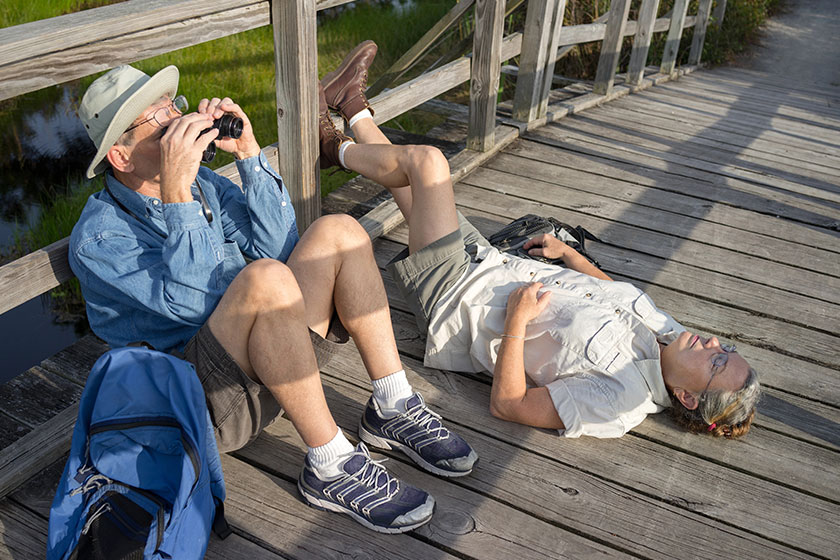Seniors birdwatching and relaxing on old wooden foot bridge