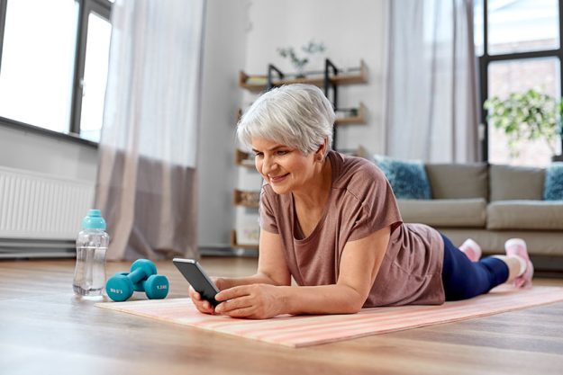 Sport-fitness-healthy-lifestyle-concept-smiling-senior-woman-smartphone-exercising Smiling senior woman with smartphone exercising on mat