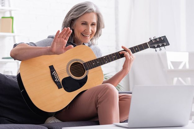 Middle aged woman with grey hair holding acoustic guitar while waving