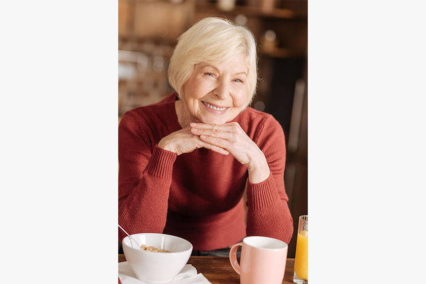Portrait of cheerful elderly woman having breakfast