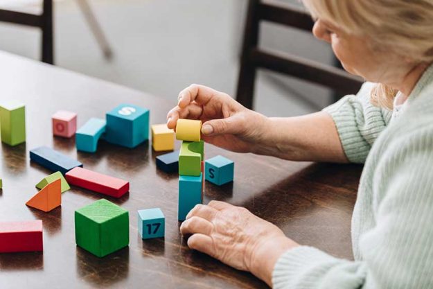 Senior woman playing with wooden cubes on table Senior woman playing with wooden cubes on table