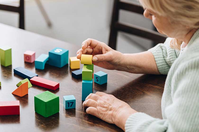 Senior woman playing with wooden cubes on table Senior woman playing with wooden cubes on table