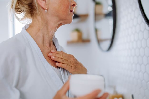 Beautiful senior woman in bathrobe applying natural cream