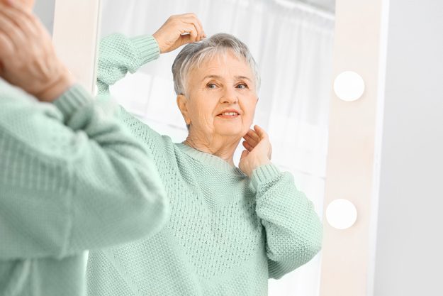 Happy senior woman looking at her reflection in mirror Happy senior woman looking at her reflection in mirror