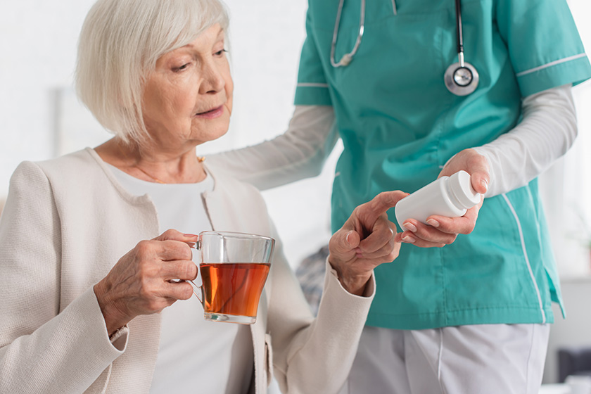 Nurse holding pills near senior patient with tea in nursing home Nurse holding pills near senior patient with tea in nursing home