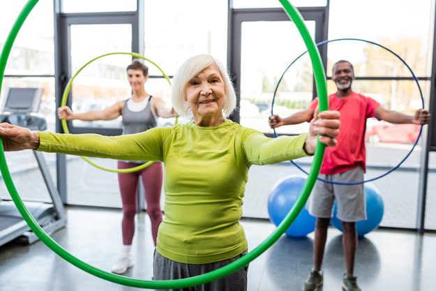 Senior woman smiling at camera while training with hula hoop in gym Senior woman smiling at camera while training with hula hoop in gym