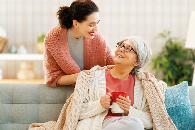 Beautiful mother and daughter are talking and smiling while sitting on couch at home. Beautiful mother and daughter are talking and smiling while sitting on couch at home.