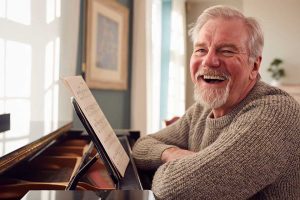 Portrait Of Senior Man At Home Enjoying Learning To Play Piano