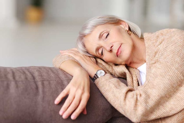 Relaxed middle aged female leaning on hand and having sweet daytime nap on soft couch at home