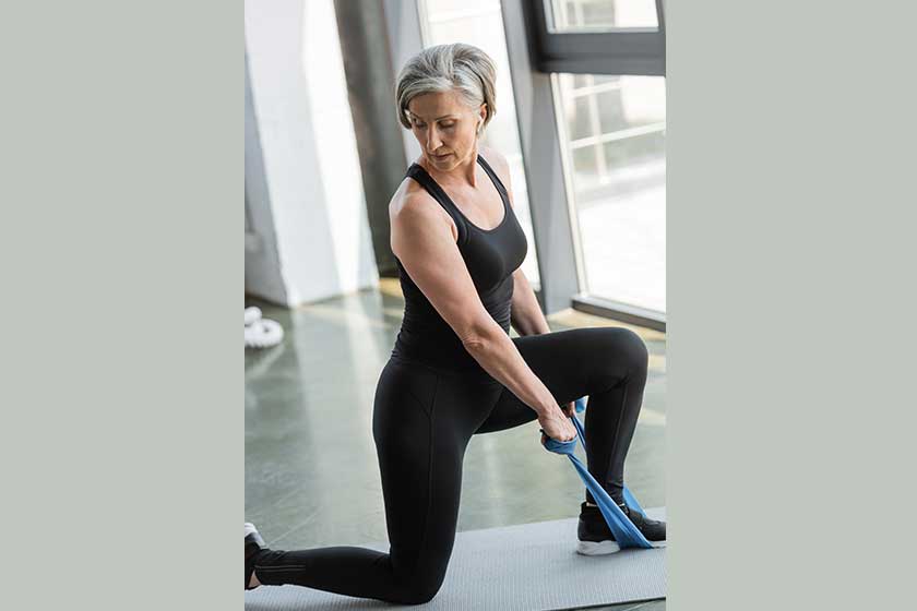 Senior woman in black leggings and tank top working out with resistance band in sports center