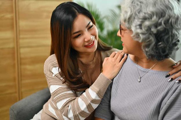 Smiling asian adult daughter with mature mother chatting and relaxing on couch at home Smiling asian adult daughter with mature mother chatting and relaxing on couch at home