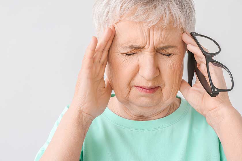 Stressed senior woman suffering from headache on light background