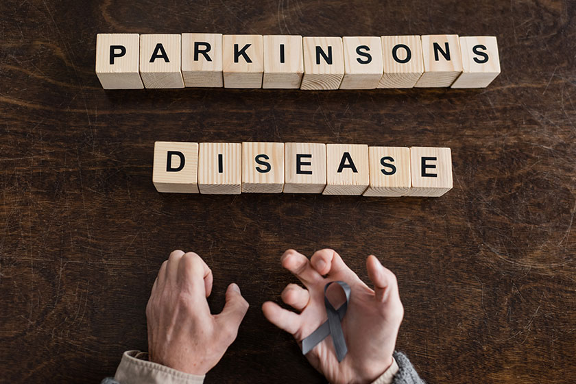 Top view of cropped man holding grey ribbon in trembling hands near blocks with parkinsons disease inscription on wooden surface Top view of cropped man holding grey ribbon in trembling hands near blocks with parkinsons disease inscription on wooden surface