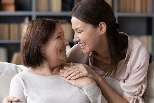 Young woman embracing from back sitting on sofa older mother. Young woman embracing from back sitting on sofa older mother.