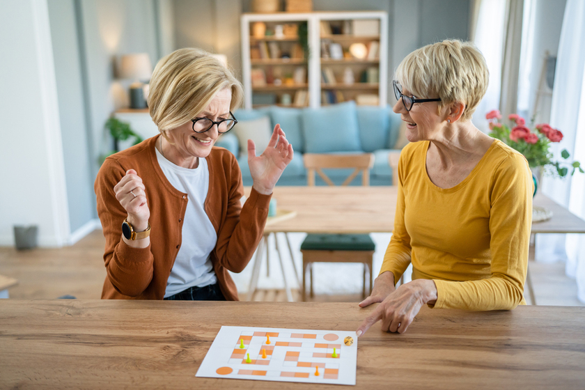 two senior women friends or sisters play leisure board game at h