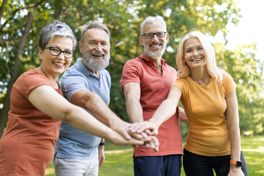 Group of cheerful senior people stacking hands after sport workout outdoors