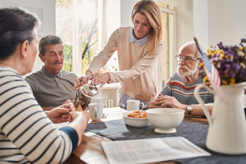 Woman holding teapot and pouring tea for the three pensioners