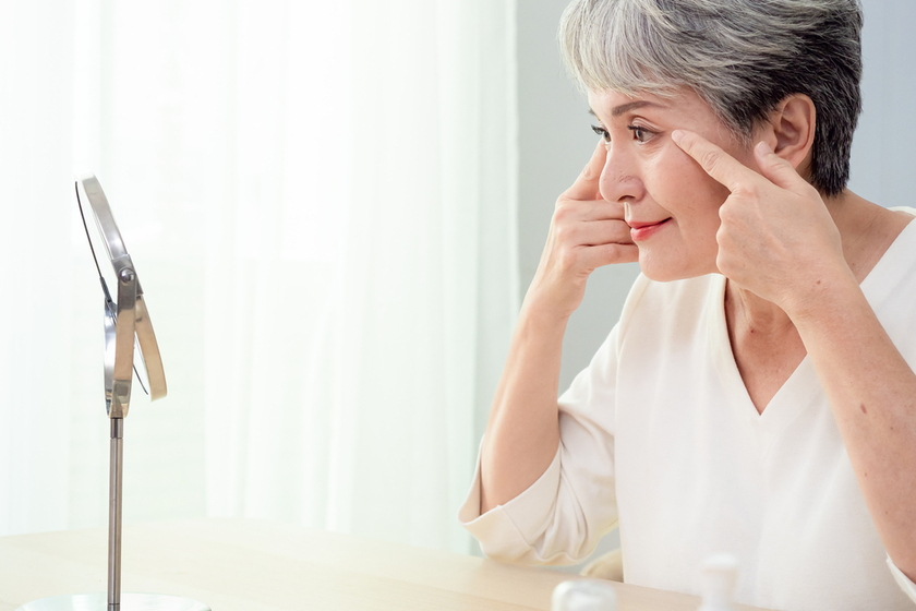 Happy 50s middle aged asian woman touching face skin looking in mirror reflection. Smiling mature old lady pampering, healthy moisturized skin care, aging beauty, skincare treatment cosmetics concept. Happy 50s middle aged asian woman touching face skin looking in mirror reflection. Smiling mature old lady pampering, healthy moisturized skin care, aging beauty, skincare treatment cosmetics concept.