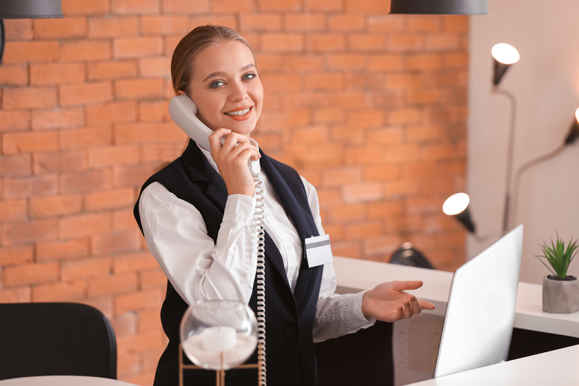 Young female receptionist talking by telephone at desk in hotel