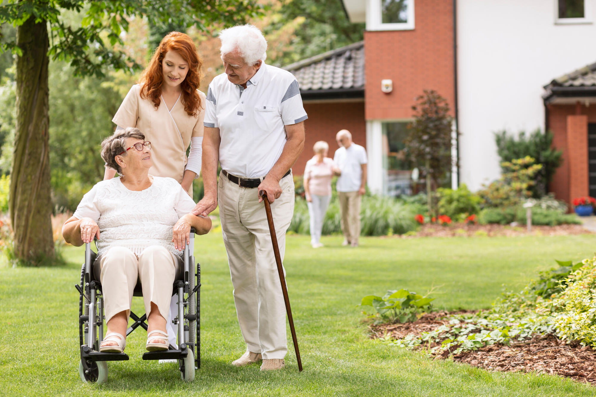 An,Elderly,Disabled,Couple,With,Their,Caretaker,In,The,Garden