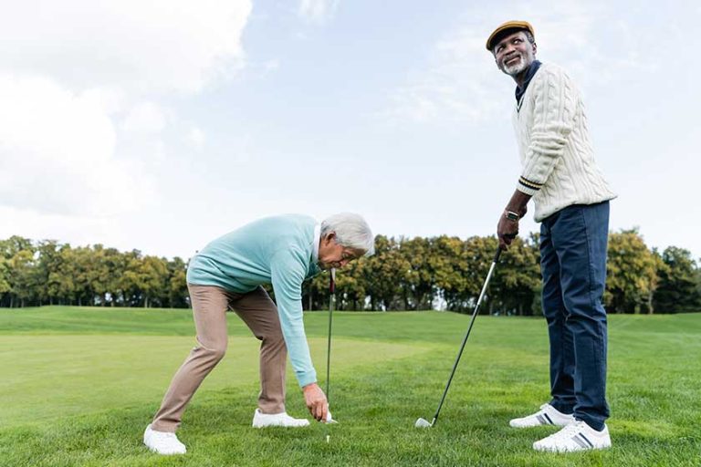 Asian-senior-man-putting-ball-golf-tee-african-american-friend