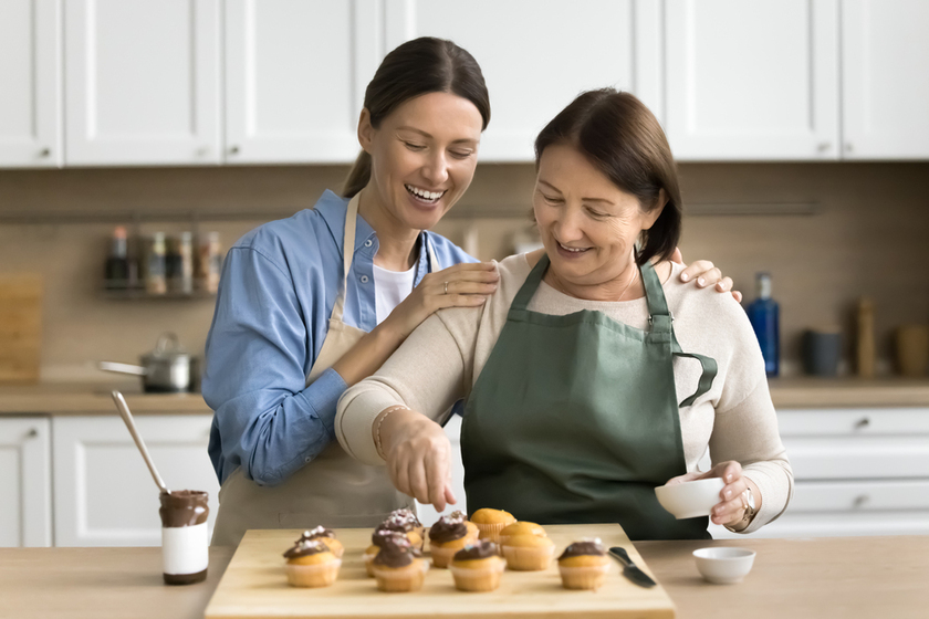 Cheerful confectioner mom and adult daughter woman decorating homemade cupcakes
