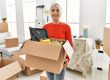 Middle age grey-haired woman smiling confident holding package at new home