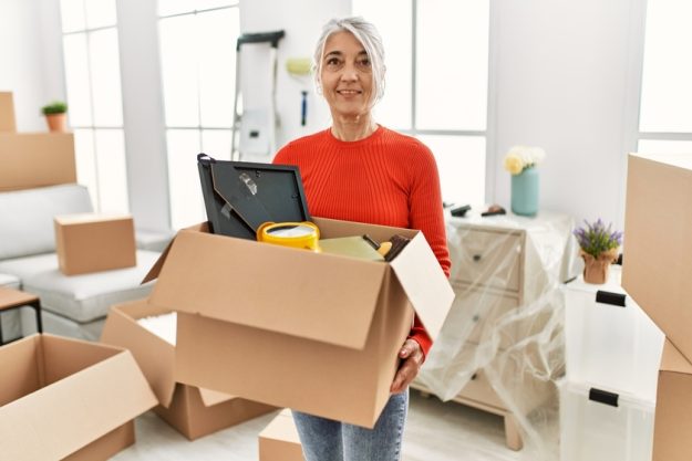 Middle age grey-haired woman smiling confident holding package at new home Middle age grey-haired woman smiling confident holding package at new home