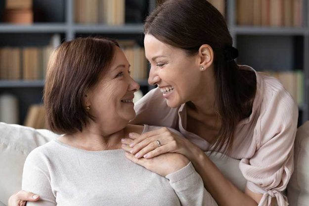 Young-woman-embracing-from-back-sitting-on-sofa-older-mother Young-woman-embracing-from-back-sitting-on-sofa-older-mother