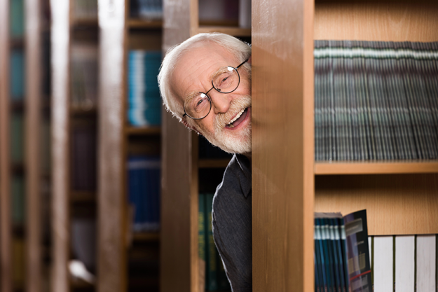 happy-grey-hair-librarian-looking-out-shelf
