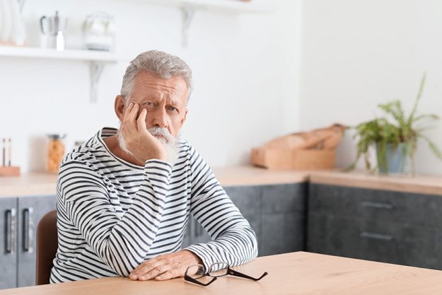Thoughtful mature man sitting at table in kitchen