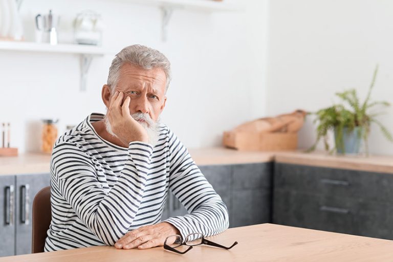 Thoughtful mature man sitting at table in kitchen