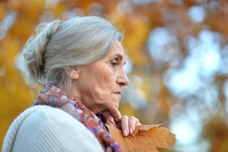 Portrait of beautiful sad senior woman on blurred autumn background