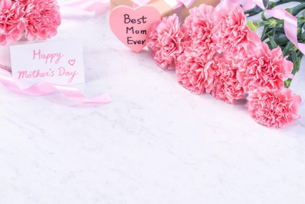 Design concept – Beautiful bunch of carnations on marble white background, top view, copy space, close up, mock up. Mothers day gift idea inspiration.