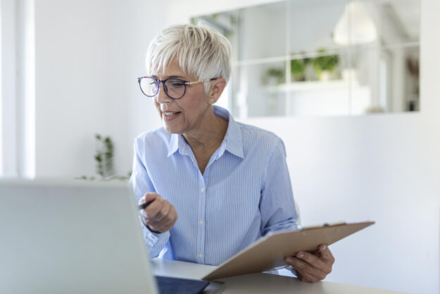 Elderly woman working on laptop computer, smiling. Woman Working From Home On Laptop In Modern Apartment. Trendy woman working on laptop from home