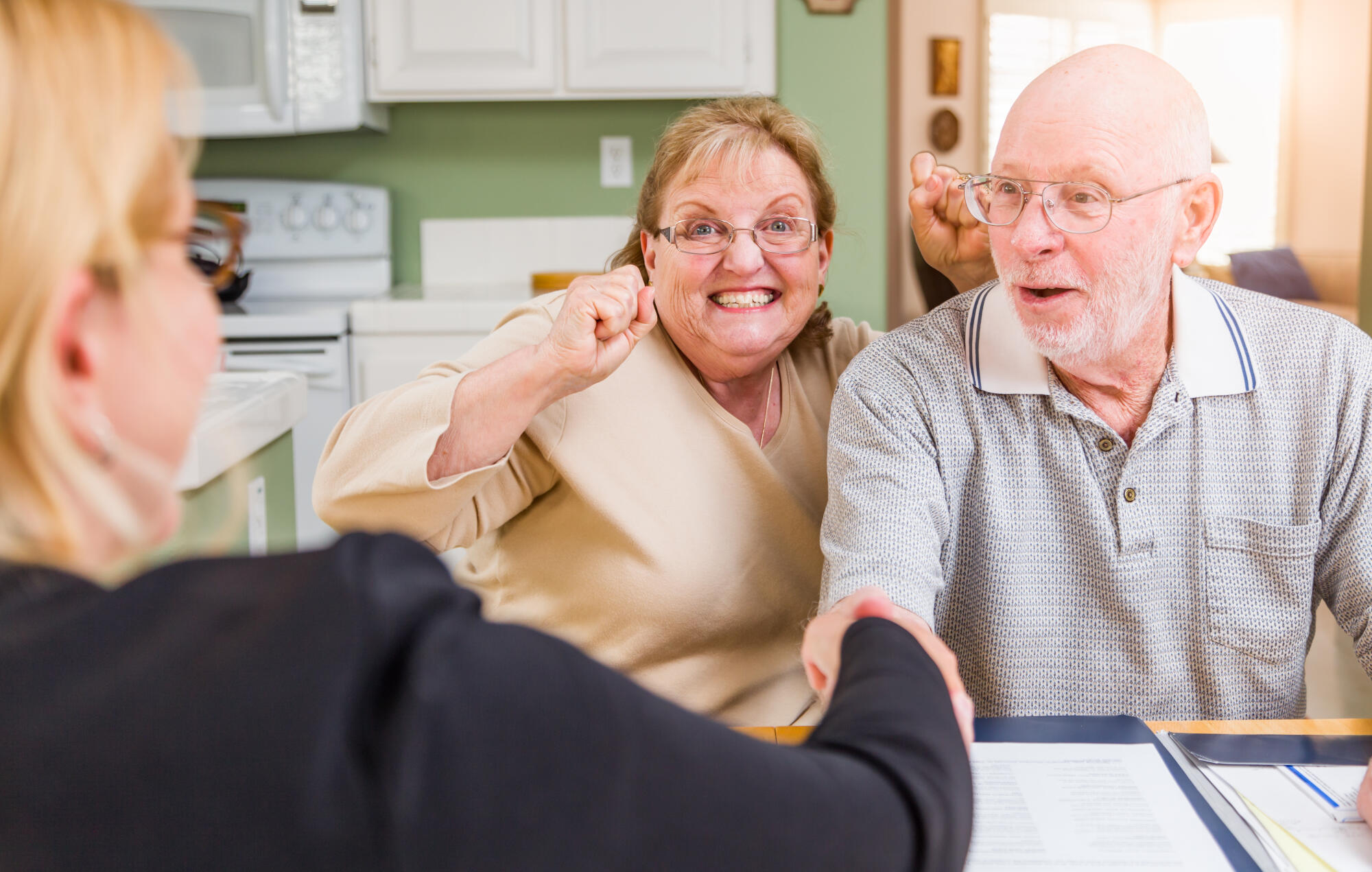 Senior Adult Couple Celebrating Over Documents in Their Home with Agent At Signing.
