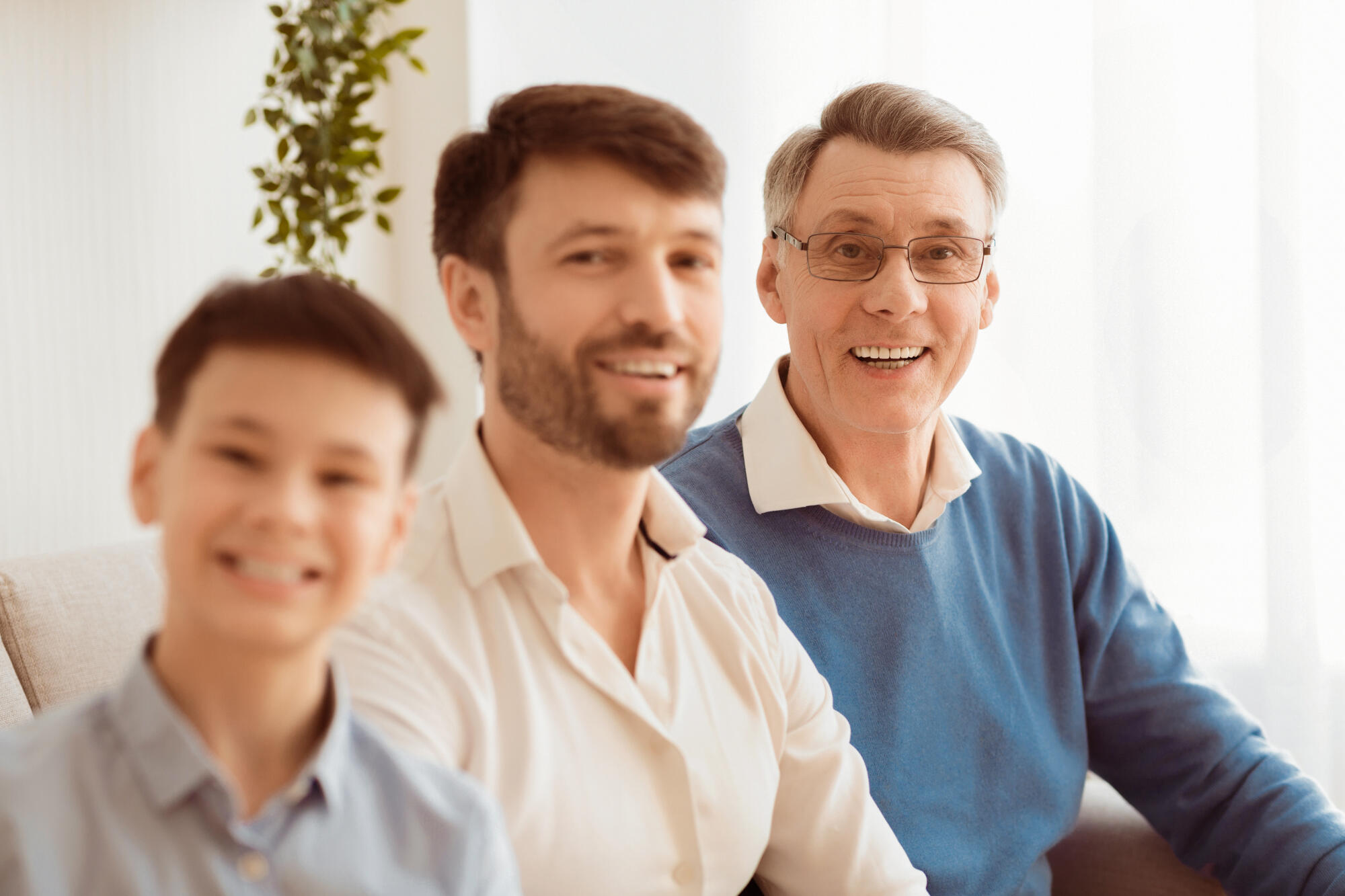 Senior Man, Son And Grandson Sitting On Sofa At Home