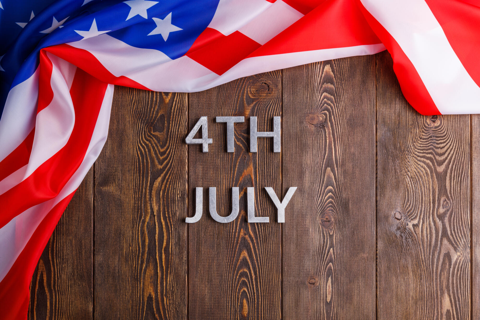 the words 4th july and crumpled usa flag on flat textured wooden surface background